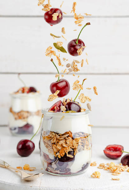 parfait de granola com iogurte grego e cerejas doces em fundo de madeira branca. alimentação saudável, espaço de cópia. - granola oatmeal cereal fruit - fotografias e filmes do acervo