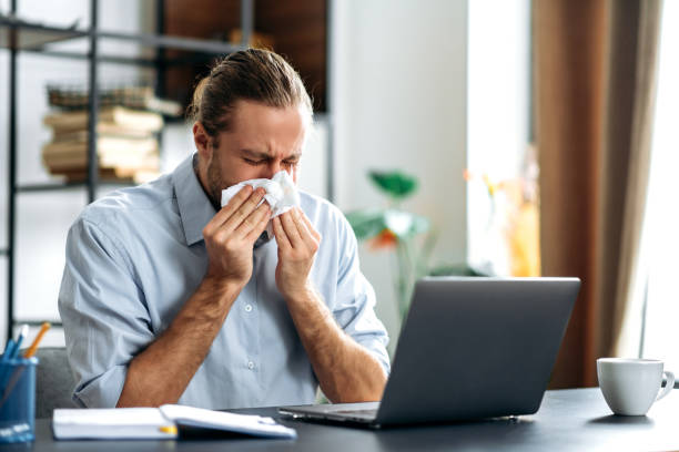 istock Male manager or freelancer sit at the desk at home office, working distantly, using paper tissue, sneezing. Caucasian unhealthy man feeling unwell, sick with running nose, need a rest 1304609945