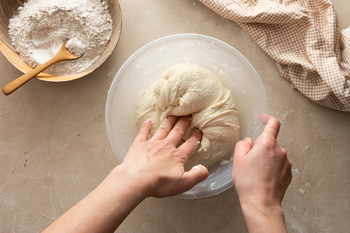 Close up shot of an unrecognizable woman kneading the dough on the work table in her kitchen. She is preparing the homemade bread.