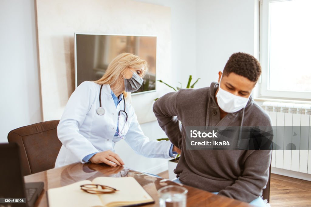 Young African-American man complained of kidney pain. Young African-American man being examined by female doctor in a doctor's office. Man with protective face mask complained of kidney pain. Kidney - Organ Stock Photo