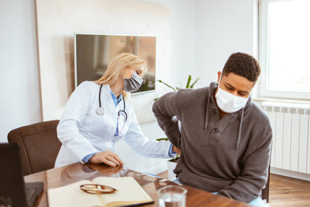 Young African-American man complained of kidney pain. Young African-American man being examined by female doctor in a doctor's office. Man with protective face mask complained of kidney pain. nephropathy photos stock pictures, royalty-free photos & images