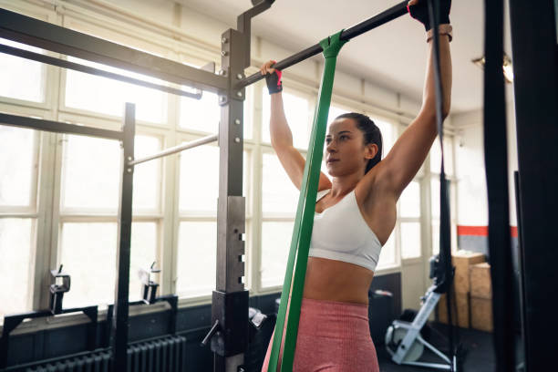 Young fit woman doing resistance band assisted pull-ups in gym Young fit woman doing resistance band assisted pull-ups exercise in gym. chin ups photos stock pictures, royalty-free photos & images