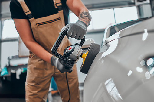 Hands with orbital polisher in auto repair shop. Focus on hands. Cropped photo.