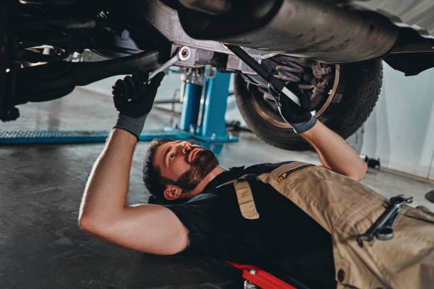 istock Handsome mechanic in uniform is working in auto service with wrenches. Man on portable plastic repair creeper. 1304619413