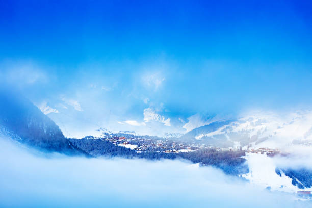 French Courchevel ski resort village, valley through the mist of Alps mountain over peaks and blue sky