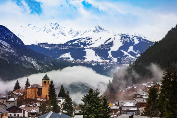 French alpine village with old church in clouds Champagny-en-Vanoise village panorama with mist and clouds around old church, over Courchevel resort on background courchevel stock pictures, royalty-free photos & images