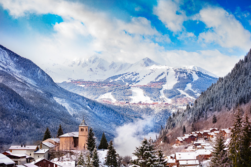 Panorama of Champagny-en-Vanoise village with mist and clouds around old church, over Courchevel resort on background