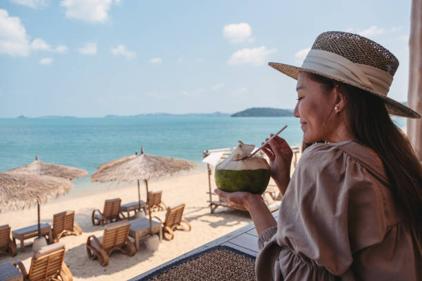 a beautiful young asian woman holding and drinking coconut juice in the beach cafe