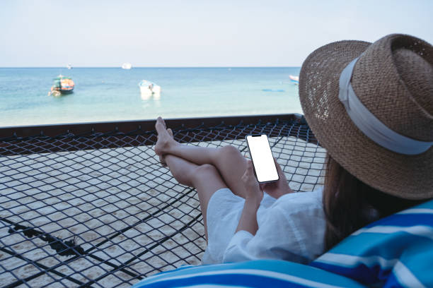 istock a woman holding mobile phone with blank desktop screen while lying down on hammock on the beach 1304635318
