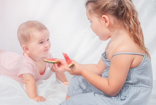 Children eat watermelon. Big sister treats baby with watermelon