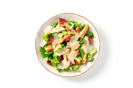 Caesar salad with grilled chicken meat, romaine and Parmesan, shot from the top on a white background