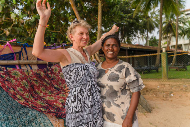 Shopping in the open-air clothing shop on a beach in Sri Lanka compras en una playa. la mujer europea, una turista, está probando un nuevo pareo en la pequeña tienda al aire libre, y la mujer india local, la vendedora y propietaria de la tienda, la está ayudando a elegir, y está demostrando la mercancía.