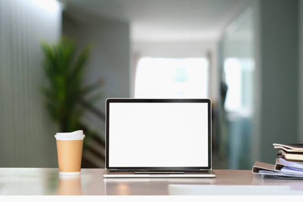 istock Front view of computer laptop with blank screen, coffee cup and document on white table in living room. 1304654137