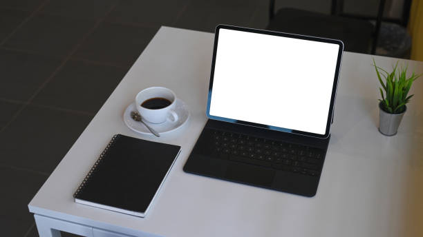 istock Mock up digital tablet with wireless keyboard, coffee cup, notebook and house plant on white table. 1304654259