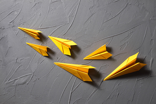 Yellow paper airplanes flying out on a gray background. Copy space