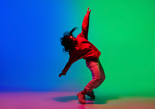 Elegante chica deportiva bailando hip-hop con ropa elegante sobre fondo colorido en el salón de baile con luz de neón. Cultura juvenil, movimiento, estilo y moda, acción. photo