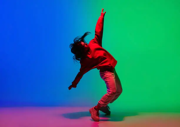 Inspiration. Stylish sportive girl dancing hip-hop in stylish clothes on colorful background at dance hall in neon light. Youth culture, movement, style and fashion, action. Fashionable bright portrait.