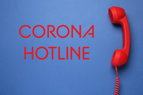 istock Covid-19 Hotline. Red handset and text on blue background, top view 1304674490