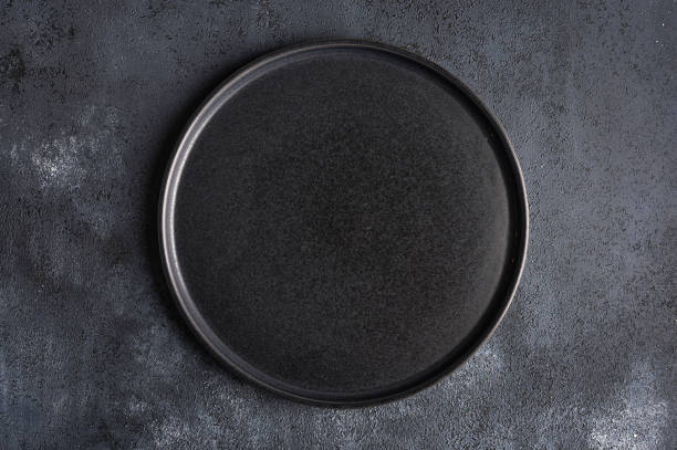 istock Empty round black plate on dark moody dark background with copy space 1304675977