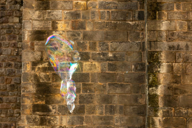 uma bolha de sabão cor de arco-íris voa contra o fundo de uma antiga parede de alvenaria. - leachate - fotografias e filmes do acervo