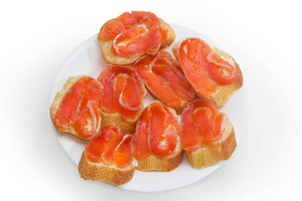 Small open sandwiches made with salted salmon slices, baguette and butter on white dish on a white background