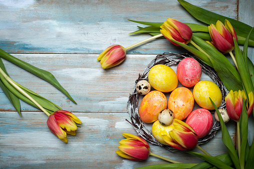 Painted Easter eggs with red and yellow tulips arrangement on a wooden table flat lay top view with copy space