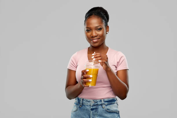 feliz mujer afroamericana bebiendo jugo de naranja - drinking straw drinking juice women fotografías e imágenes de stock