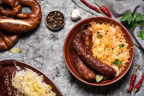Smoked sausages served with cooked sauerkraut sour cabbage on a plate tabletop view with food ingredients