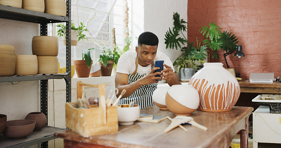 Shot of a young man taking pictures of his finished products with a smartphone in a pottery studio