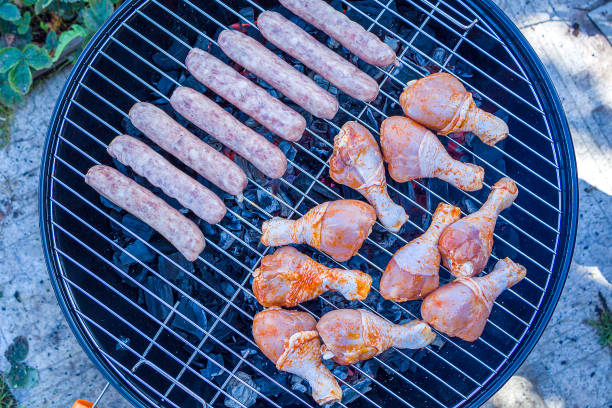 istock Process cooking chicken drumstick and sausages on barbecue grill outdoors. Picnic, eating outdoors. Metal barbecue grill (brazier). Raw meat 1304688992