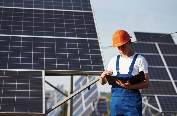 istock Stands with notepad. Male worker in blue uniform outdoors with solar batteries at sunny day 1304691373
