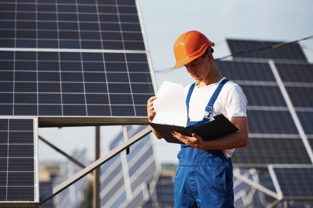 istock Stands with notepad. Male worker in blue uniform outdoors with solar batteries at sunny day 1304691470