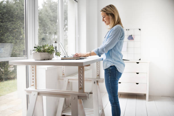 Businesswoman working at ergonomic standing workstation. Businesswoman working at ergonomic standing workstation. ergonomics stock pictures, royalty-free photos & images