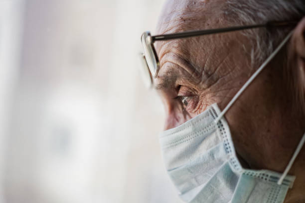 istock Aged man with face mask and eyeglasses on forehead looking through window. 1304693050