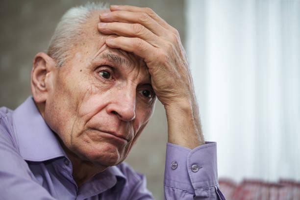 istock Pensive old man sitting at home looking with sad and holding hand on forehead. 1304693064