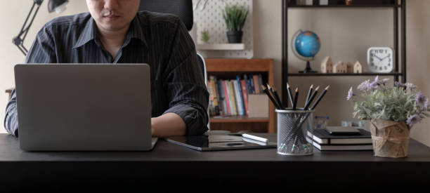 Asian freelancer business man working at home using laptop computer at workspace office desk in living room. Remote work from home. stock photo