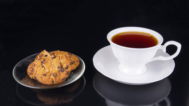 weiße tasse tee mit gebissenen haferflocken kekse auf schwarzem hintergrund - english breakfast tea stock-fotos und bilder