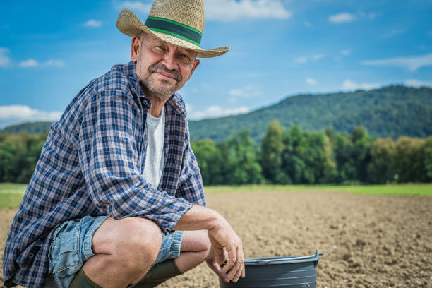 Portrait of mature male farmer with bucket crouching in field.