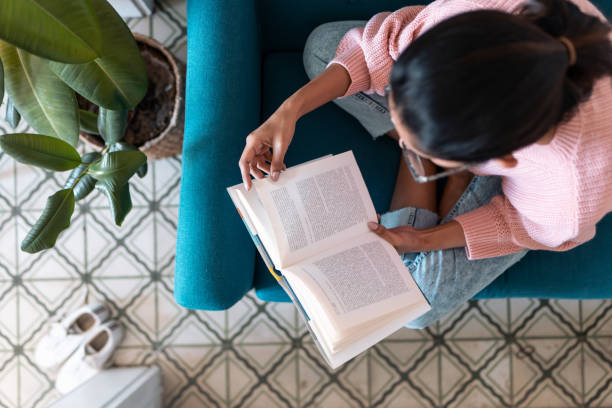 istock Pretty young woman reading a book while sitting on sofa at home. Top view. 1304695836