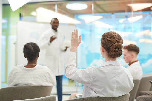 Back view at young people raising hands while listening to medical seminar in college, copy space