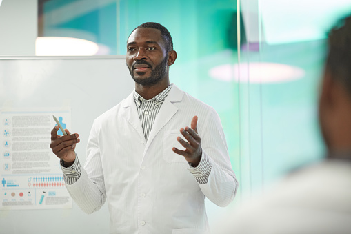 Waist up portrait of African-American man standing by whiteboard while giving presentation during medical seminar in college, copy space