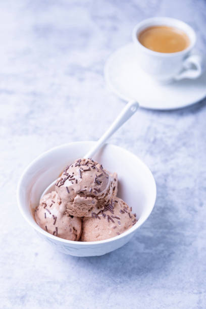 istock Chocolate ice cream with chocolate topping in a white bowl on a light background. Three scoops of homemade ice cream and a cup of coffee. 1304700353