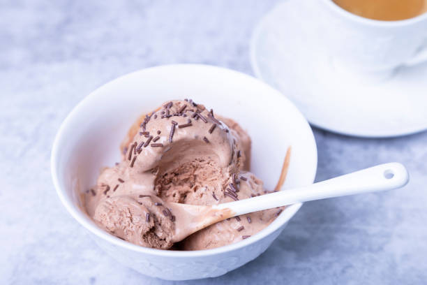 istock Chocolate ice cream with chocolate topping in a white bowl on a light background. Three scoops of homemade ice cream and a cup of coffee. 1304700373