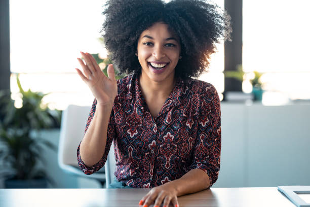istock Beautiful afro young woman waving hand while doing video call looking at camera in the office. 1304702057