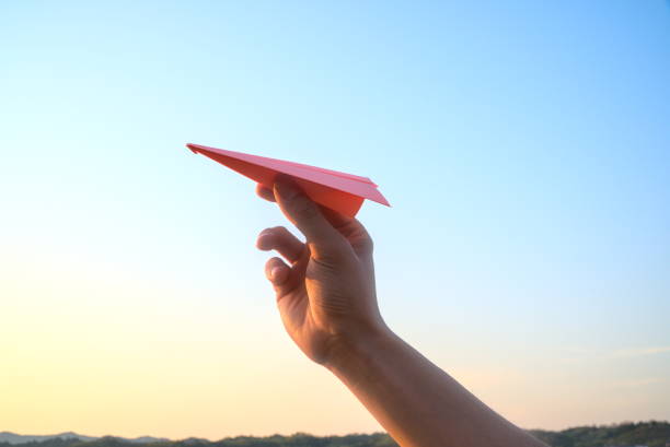 istock Hand holding a pink paper airplane on sunrise sky background 1304702612