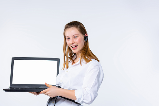 Young blonde with earphone in the ear. Shows a white laptop screen to the camera. White background. High quality photo