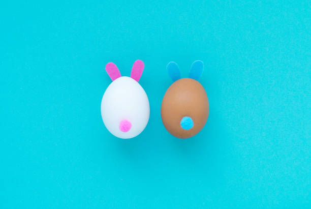 istock Easter eggs with pink and blue bunny ears and tails on a light blue background. Minimal Easter concept. Imitation rabbit. Postcard. Flat lay, top view 1304702768