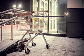Empty shopping cart sits on the steps outside the store on a snowy winter evening