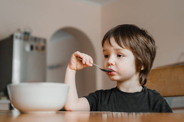 istock A cute little boy holding a spoon and having having breakfast at home 1304708764