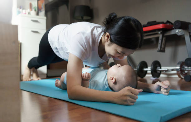 Happy Smiling Sporty Asian young mother doing plank exercise with her baby boy at home. Healthy Mom training and practicing yoga with her son on floor in bedroom. Happy Smiling Sporty Asian young mother doing plank exercise with her baby boy at home. Healthy Mom training and practicing yoga with her son on the floor in bedroom. asian mom exercise stock pictures, royalty-free photos & images